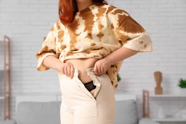 Image of woman trying to do her trousers up after pregnancy weight gain Bishops Stortford