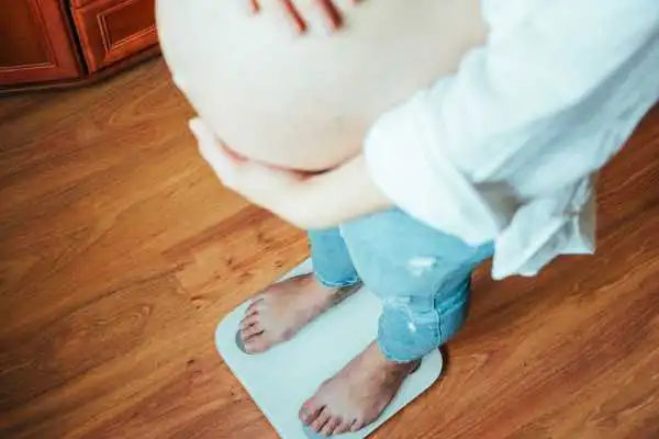 Image of woman weighing herself and experiencing weight gain through pregnancy Bishops Stortford